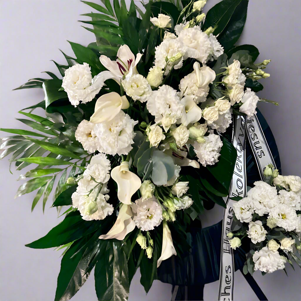 Apvalus, didelis gedulo vainikas - puoštas baltomis kalijomis, karališka balta eustoma, sodria žaluma ir šviesiai žalio eukalipto akentais.
